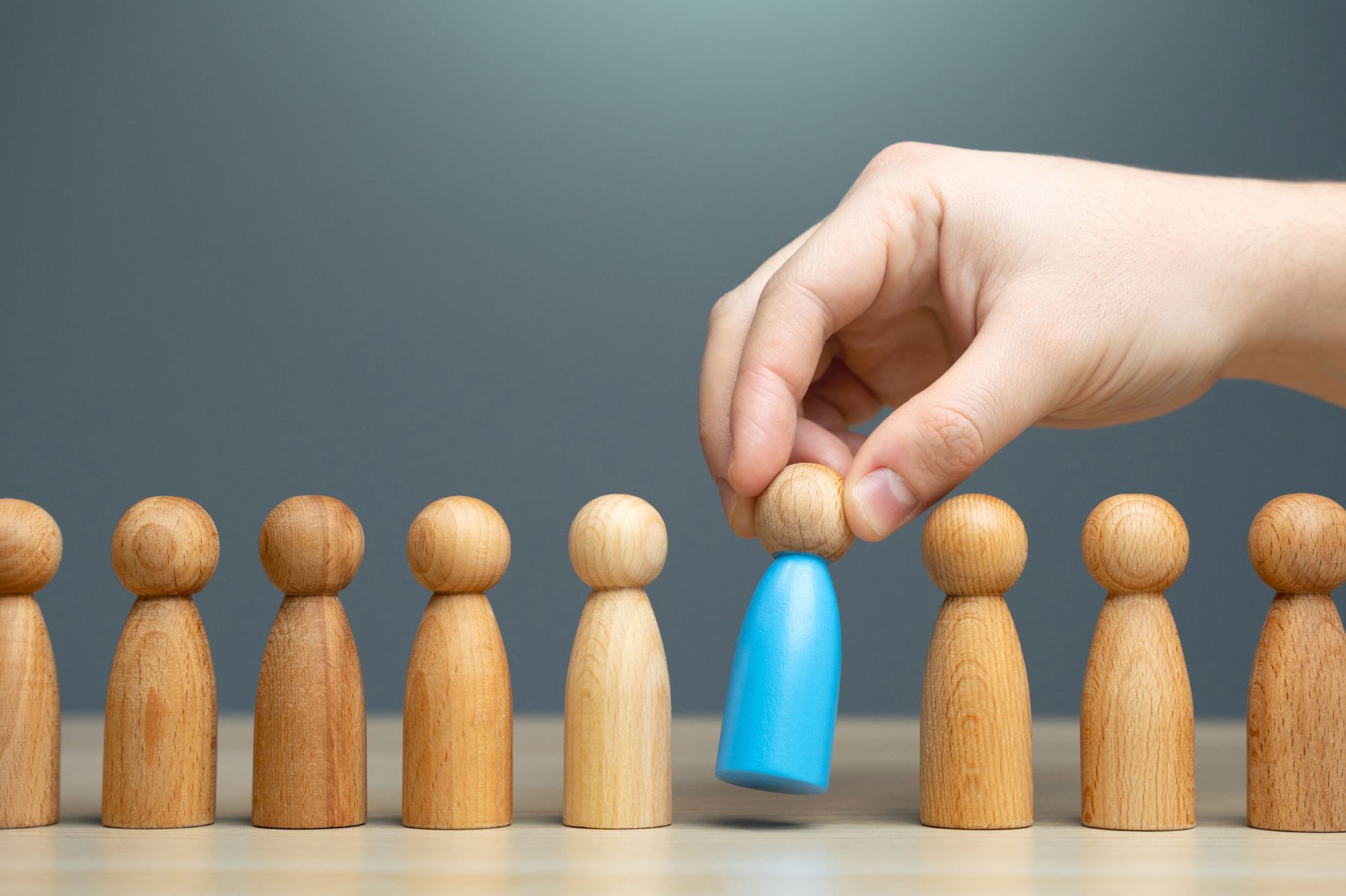 Hand selecting a blue wooden figure among others, symbolizing the process of how to choose a family business advisor who aligns with family and business needs.