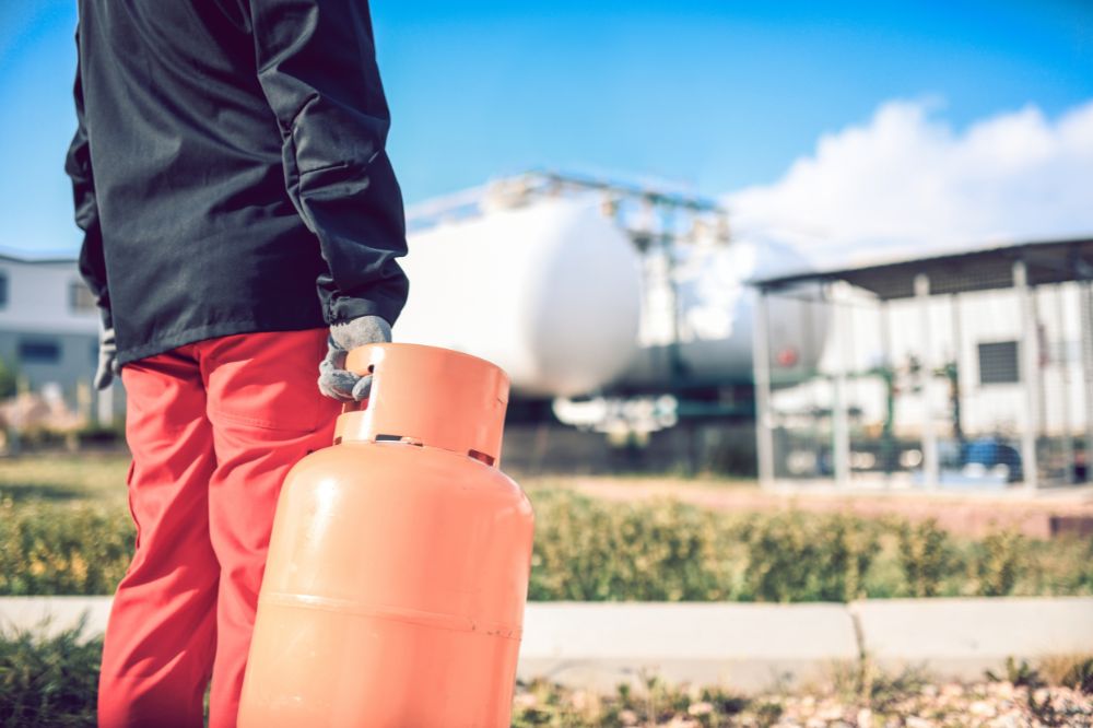 Preparing a Gas Distribution Business for Sale A worker holding an orange propane cylinder at a gas distribution facility, representing ownership transition and succession planning in the fuel and propane industry.