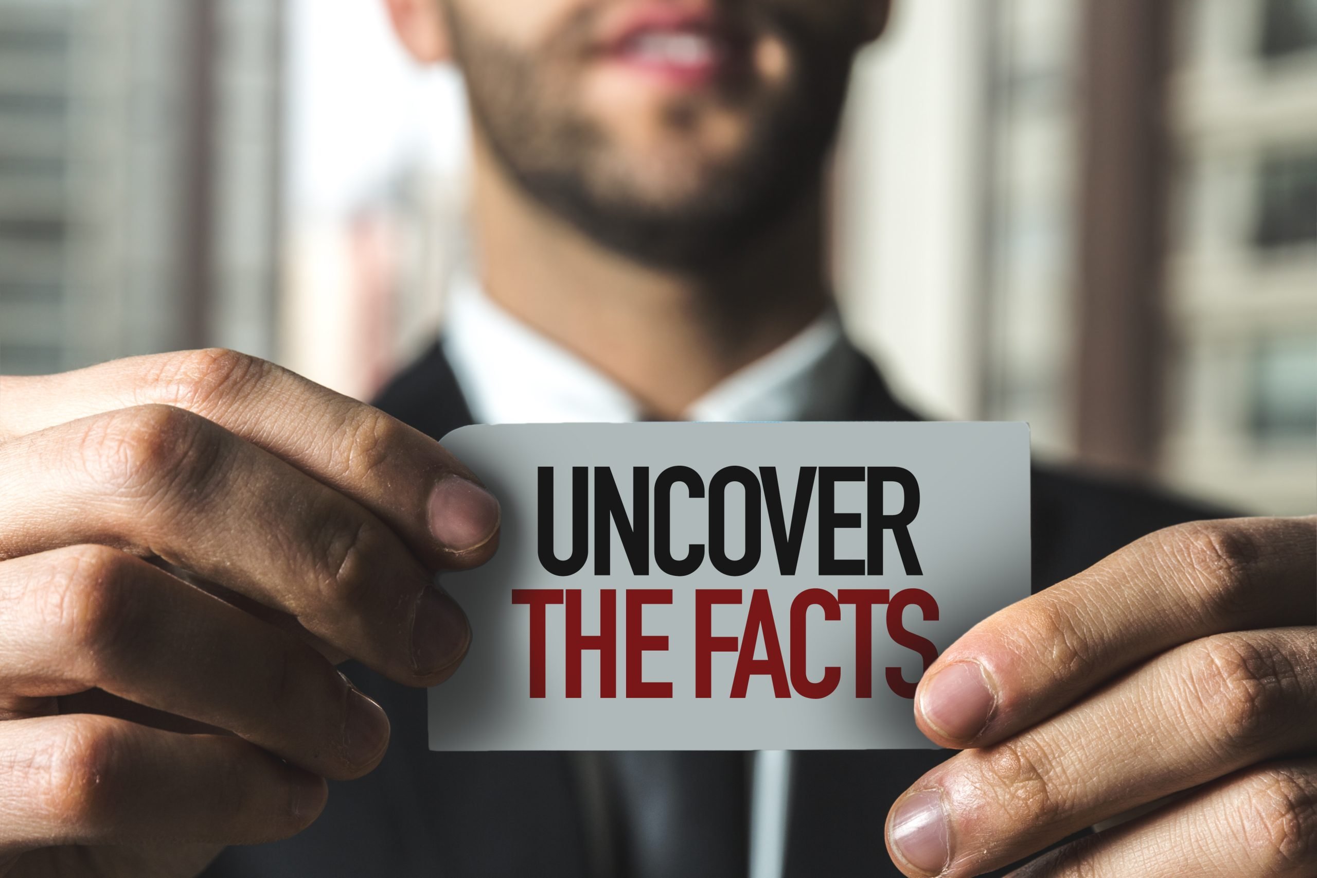 Close-up of a businessman holding a card that reads uncover the facts, symbolizing misconceptions and what family business owners get wrong about advisors.